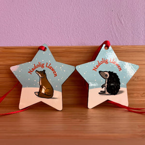 Two star-shaped ornaments with animals and 'Nadolig Llawen' text on a wooden surface.