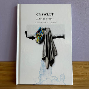 Book titled 'CYSWLTT' by Jadwiga Grabos on a wooden surface with a purple wall background