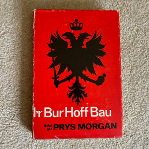 Red book cover with black emblem and text on a beige carpet background