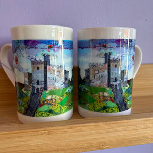 Two mugs with castle design on a wooden surface and purple wall background