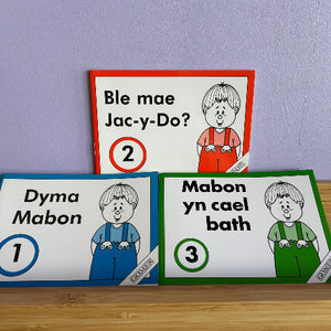 Three books with cartoon characters and text on a wooden surface and purple wall background.