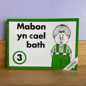 Children's book with a cartoon character and text on a green border, placed on a wooden surface with a purple wall background.
