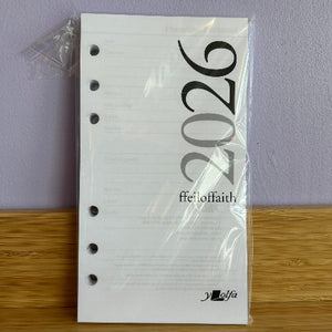 White planner refill with '2026' printed on it, held in place by a clear plastic bag against a purple wall.