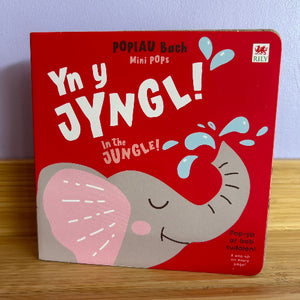 Children's book titled 'Yn y Jyngl! In the Jungle!' with an elephant illustration on a red background.