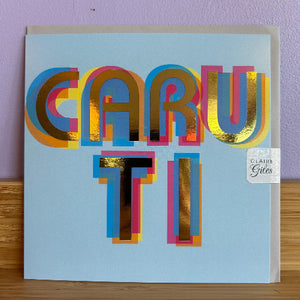 Colorful card with 'CARU TI' text on a light blue background, featuring gold, pink, and blue colors.