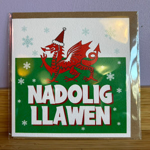 Card with a red dragon wearing a Santa hat and the text 'Nadolig Llawen' on a green background.