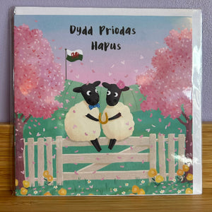 Card with two sheep on a fence and trees in the background, featuring Welsh text.