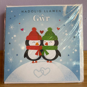 Christmas card with penguins wearing scarves and hats on a snowy background, featuring the text 'Nadolig Llawen Gŵr'.