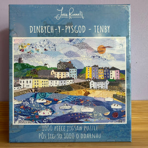 Jigsaw puzzle box with a colorful illustration of a town by a river, featuring the brand 'Josie Russell'.