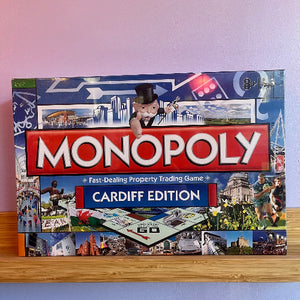 Monopoly Cardiff Edition board game box on a wooden surface with a light purple background