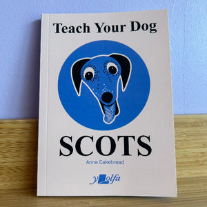 Book titled 'Teach Your Dog SCOTS' by Anne Cakebread on a wooden surface with a blue background