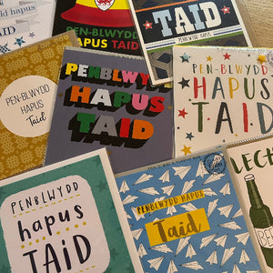 Collection of greeting cards with 'PEN-BLWYDD HAPUS TAID' text on a wooden surface.