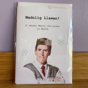 Card with a man wearing a crown and text 'Nadolig Llawen! It means Merry Christmas in Welsh' on a purple background.