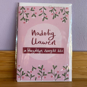 Card with 'Nadolig Llawen' text on a pink background with green leaves and hearts.