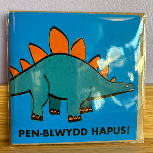 Card with a cartoon dinosaur on a blue background, featuring the text 'Pen-Blwydd Hapus!'.