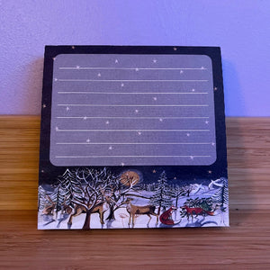 Note pad with winter scene design featuring reindeer and trees on a wooden surface.