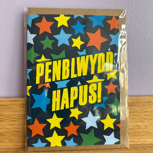 Greeting card with colorful star pattern and 'PENBLWYDD HAPUS!' text on a wooden surface.