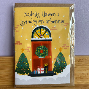 Greeting card with Christmas design featuring trees, presents, and a wreath on a yellow background.