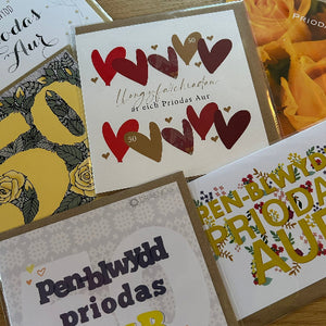 Collection of greeting cards with heart designs and Welsh text on a wooden surface.