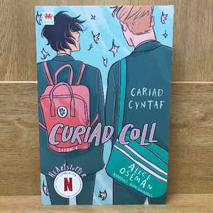 Book cover of 'Cariad Cyntaf, Curiad Coll' with two characters and a pink backpack on a wooden surface.