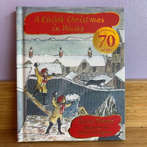 Book titled 'A Child's Christmas in Wales' celebrating 70 years on a wooden surface with a purple wall background.
