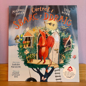 Book cover of 'Cartref i Sbarc y Ddraig' with a red dragon character on a treehouse against a purple background