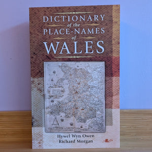 Book titled 'Dictionary of the Place-Names of Wales' on a wooden surface with a blue wall background.