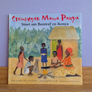 Children's book titled 'Crempogau Mama Panya' with illustrations of people around a fire on a wooden surface.