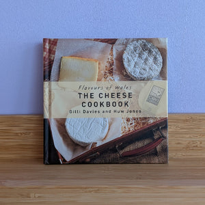 The Cheese Cookbook by Gilli Davies and Huw Jones on a wooden surface with a purple wall background