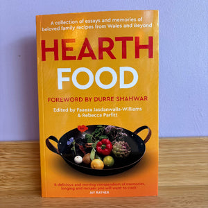 Book titled 'Hearth Food' with a yellow cover and black pan on a wooden surface.