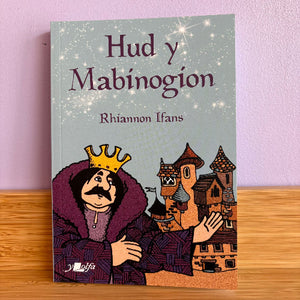 Book cover of 'Hud y Mabinogion' by Rhiannon Ifans with a character and houses illustration on a wooden surface.