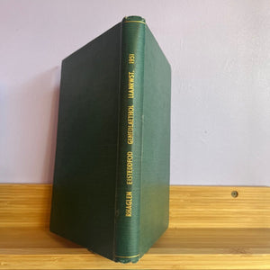Green book with gold text on a wooden surface and white wall background