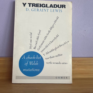 Book titled 'Y Treigladur' by D. Geraint Lewis on a wooden surface with a purple wall background