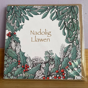 Greeting card with decorative border and 'Nadolig Llawen' text on a wooden surface.