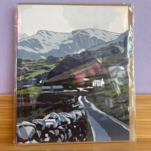 Packaged greeting card with mountain landscape design on a wooden surface.