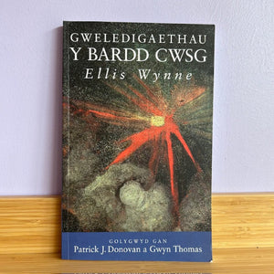 Book titled 'Gweledigaethau Y Bardd Cwsg' by Ellis Wynne on a wooden surface with a light purple wall background.