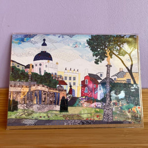 Decorative greeting card with a colorful illustration of a town scene on a wooden surface.