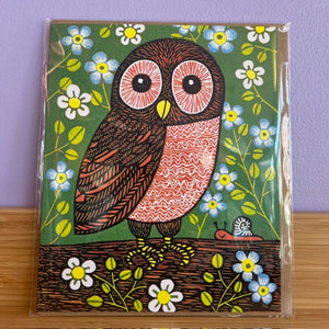 Card with a colorful owl design on a green background with flowers, against a purple wall.