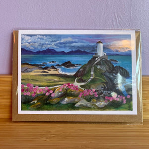Painting of a lighthouse on a coastal landscape with pink flowers, framed in gold.