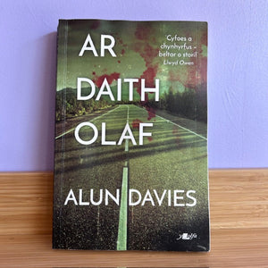 Book titled 'AR DAITH OLAF' by Alun Davies on a wooden surface with a purple wall background