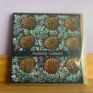 Decorative box with pine cone pattern and 'Nadolig Llawen' text on a wooden surface.