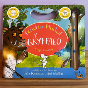 A children's magic painting book titled 'Peintio Hudo! y Gryffalo' with a built-in paintbrush in a clear window on the cover, photographed on a wooden surface against a light purple background.