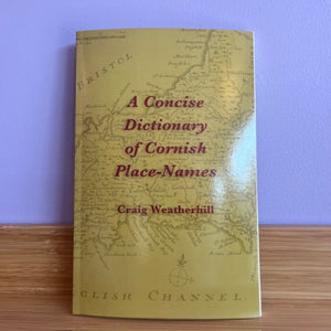 Book titled 'A Concise Dictionary of Cornish Place-Names' by Craig Weatherhill on a wooden surface with a purple background.