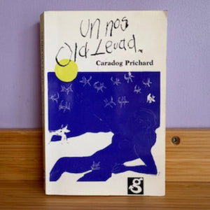Book cover with a blue illustration of a person and animals under a moon, on a wooden surface with a purple wall background.
