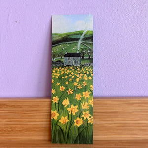 Painting of a house in a field with yellow flowers on a wooden surface and purple wall background