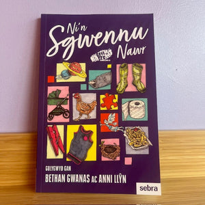 Book titled 'Nán Sgwennu Nawr' with colorful illustrations on a purple background, placed on a wooden surface.