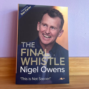 Book titled 'The Final Whistle' by Nigel Owens on a wooden surface with a purple wall background