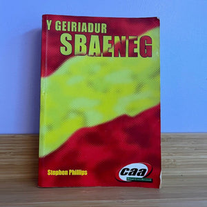 Book titled 'Y Geiriadur Sbaeneg' with a red and green cover on a wooden surface.