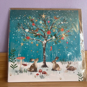 Advent calendar with a winter scene featuring a tree, rabbits, and festive elements.
