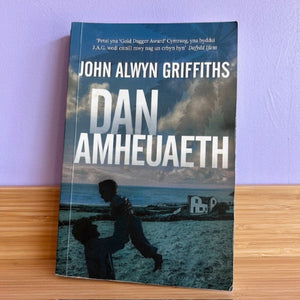 Book titled 'Dan Amheuaeth' by John Alwyn Griffiths on a wooden surface with a purple wall background.
